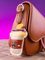 Close-up of a playful leather keychain in the shape of a coffee cup or bubble tea on a brown bag
