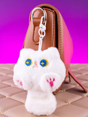 Close-up of a soft plush keychain in the shape of a white cat on a brown bag