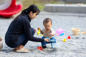 Mother playing with toddler on gravel ground