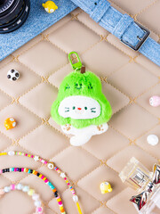 A close-up of a soft plush keychain featuring a cute and playful white kitten wearing a pear-shaped hat