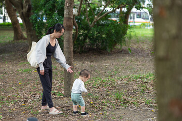 Mother guiding toddler walking outdoors in park