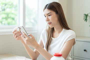 Health care asian young woman using smart phone for reading, searching prescription on bottle...