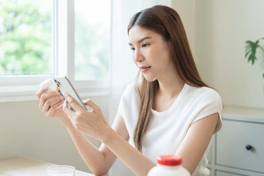Health care asian young woman using smart phone for reading, searching prescription on bottle medicine, pill label text about information online, instructions side effects, pharmacy medicament concept