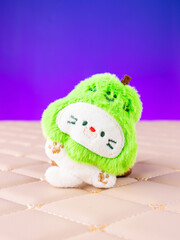A close-up of a soft plush keychain featuring a cute and playful white kitten wearing a pear-shaped hat
