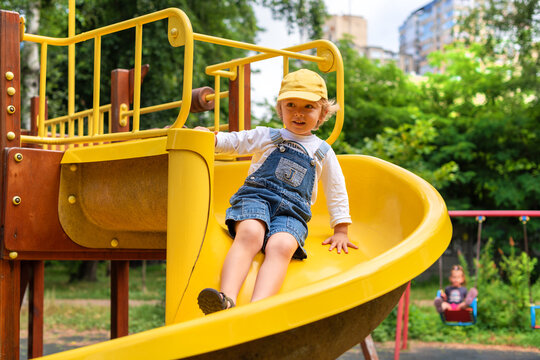 A little boy riding on a yellow slide at a playground