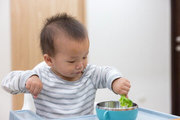 Happy baby eating fresh broccoli at home