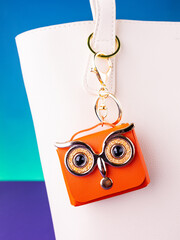 A close-up of a small orange leather mini bag featuring an owl design with bright, expressive eyes on white  bag