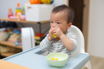 Infant sitting on high chair eating fresh corn