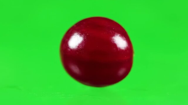 Isolated macro shot of a single perfectly round fresh red cranberry slowly rotating against a uniform vibrant green screen background vibrant, slowly, productionelement