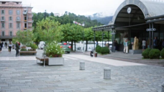 Blurred urban plaza with soft bokeh, out of focus trees, planters, benches and stone pavement, distant arched station by the lake; background backplate copyspace.