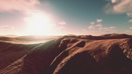 Rolling hills stretch across the horizon, bathed in warm light at dawn. Soft clouds drift above, casting gentle shadows on the rugged terrain, creating a peaceful and serene scene. © icetray