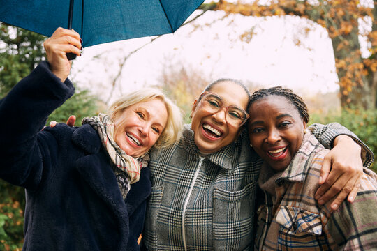 Portrait of happy mature woman with arm around female friends enjoying leisure time
