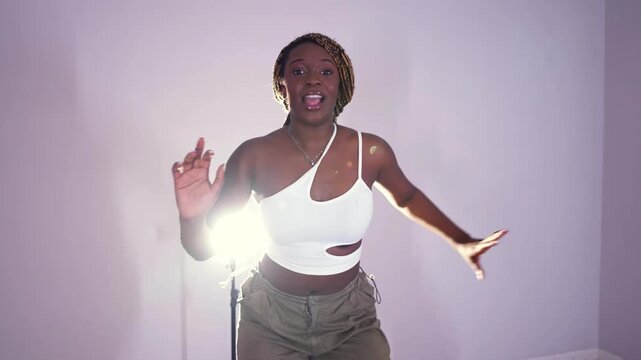 Young black woman with braided hair joyfully dancing in a studio with a bright backlight. Passionate female dancer performs modern afrobeats