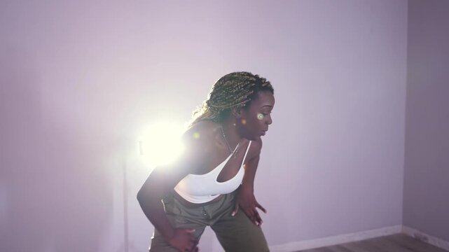 Passionate african woman with braids dancing contemporary afrobeat moves in a studio. Energetic dancer performing an intense choreography