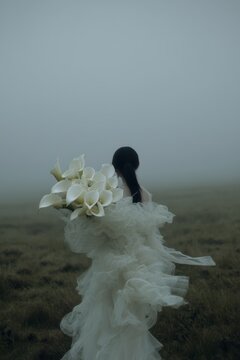Mujer de espaldas con vestido blanco de tul y ramo de calas en niebla, Estilo nupcial premium con vestido de dise&ntilde;o y ramo de calas, Publicidad de moda nupcial de lujo con espacio para texto
