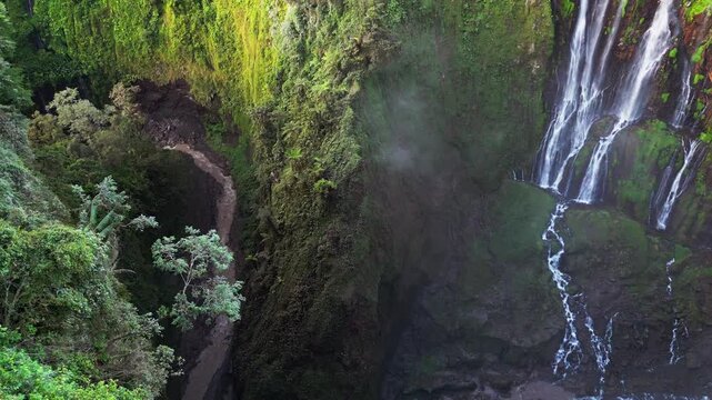 Aerial view of Tumpak Sewu Waterfall in East Java capturing numerous cascades pouring into a canyon with flowing river channels, moss covered rocks, mist filled air and dramatic tropical landscape