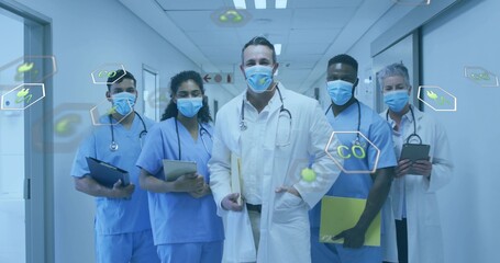 Fototapeta premium Leading lead Dr walking care team in hospital corridor, wearing lab coat, scrubs, stethoscope, mask
