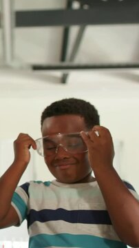 Vertical video: Raising safety goggles, boy in striped tee adjusting fit in makerspace for project