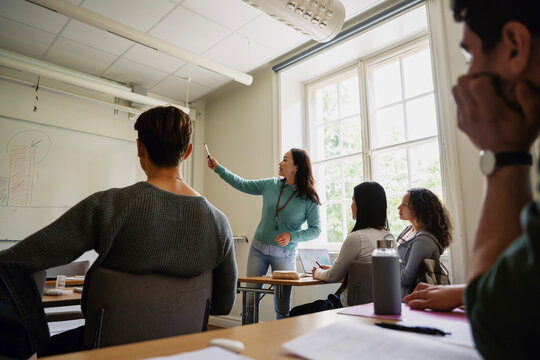 Female professor explaining bar graph to students through whiteboard in classroom at university