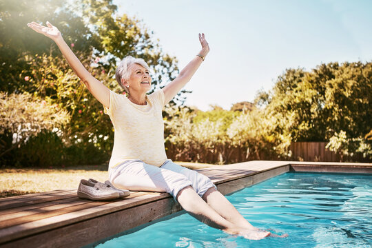 Freedom, retirement and swimming pool with old woman outdoor in garden of home for celebration. Arms raised, relax and smile with happy senior person in backyard for poolside break or stress relief