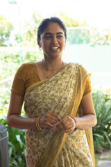 Indian woman standing on sunlit garden patio, in floral sari mustard-patterned and gold jewelry © wavebreak3