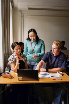 Female professor explaining query on laptop to students studying in classroom at college