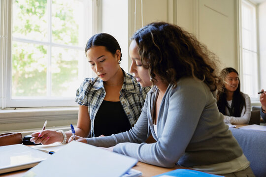 Young woman solving math equation with female friend while studying in classroom at college