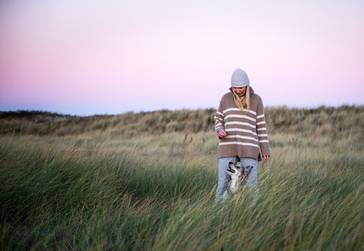 Woman walking with dog on sand dunes at sunset in autumn