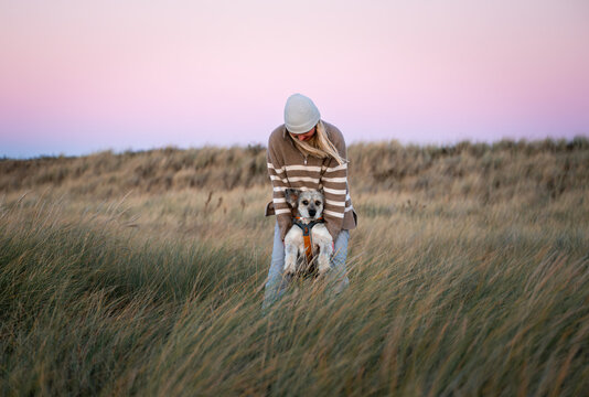 Woman holding dog in grassy field at sunset in autumn evening