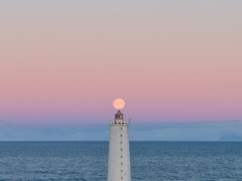 Lighthouse with full moon rising over ocean in iceland