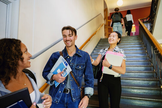 Portrait of smiling young man enjoying leisure time with female friends near staircase in university campus