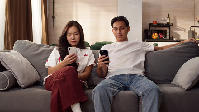 Sad ignore couple sit couch at home using smartphone. Addiction social media digital technology, relationship coldness issue. Cell mobile phone scrolling problem. Useless cellphone internet surfing.