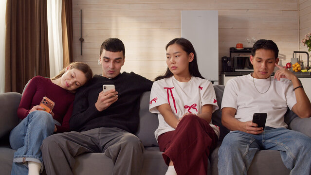 Sad ignore friends sit couch at home living room using smartphone. Addiction social media digital technology, people issue. Cell mobile phone scrolling problem. Useless cellphone internet surfing.
