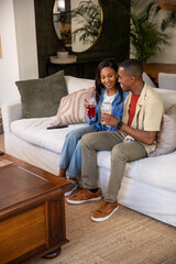 Obraz premium African American men sitting side by side on sofa in living room holding cups with straws