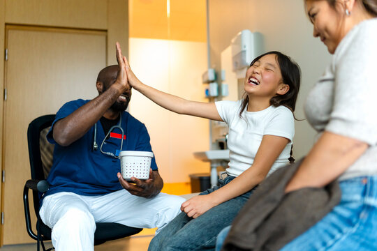 Happy girl giving high-five to male doctor during clinic visit
