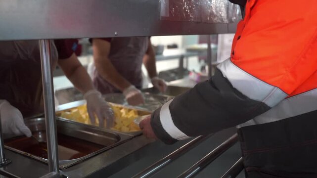 Distribution of food in the dining room. Get in line for a portion of food. The cook puts food in a tray. High quality video