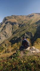 Fototapeta premium Solo Trekker Resting on Rocky Peak Enjoying Scenic Himalayan View