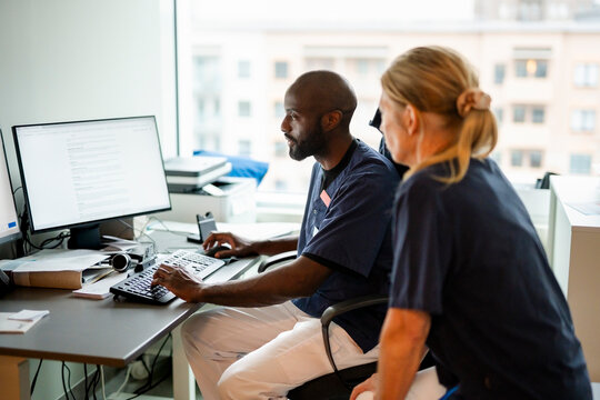 Male medical expert using computer while discussing records with female colleague in hospital office