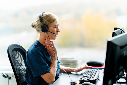 Female medical expert wearing headset assisting patient on video call through computer in clinic