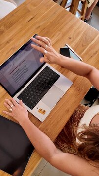 Vertical video of a woman working on her laptop and scrolling in a cafe environment 
