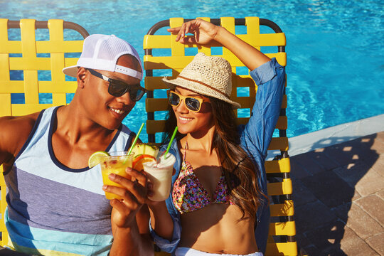Holiday, couple and cheers with cocktails at poolside for celebration, resort destination and travel. Sunglasses, people and relax at hotel with drinks toast, summer vacation and bonding in sunshine