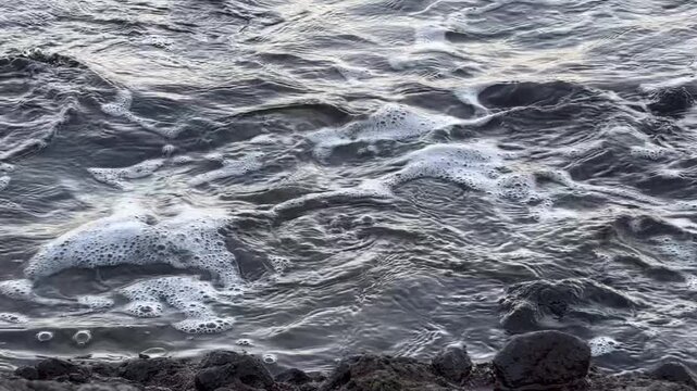 Calm ocean waves washing a rocky shore at dawn, soft pastel blue light before sunrise, minimal coastal scenery conveying freedom, travel lifestyle, nature balance, environment and relaxing seaside mor