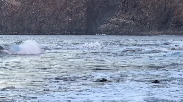 Calm ocean waves washing a rocky shore at dawn, soft pastel blue light before sunrise, minimal coastal scenery conveying freedom, travel lifestyle, nature balance, environment and relaxing seaside mor