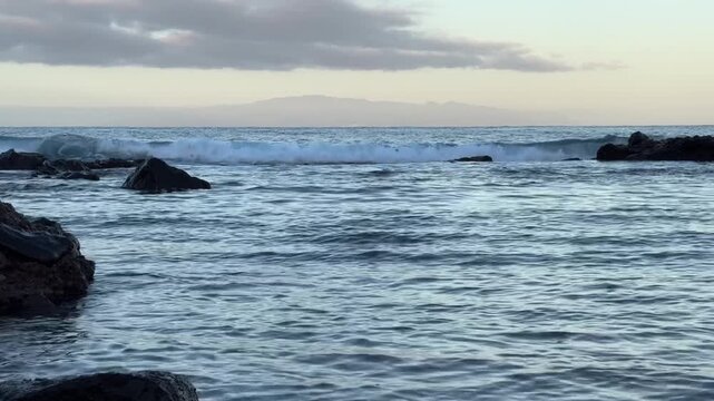 Calm ocean waves washing a rocky shore at dawn, soft pastel blue light before sunrise, minimal coastal scenery conveying freedom, travel lifestyle, nature balance, environment and relaxing seaside mor