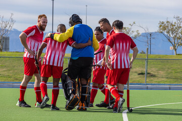 Obraz premium Diverse male field hockey teammates huddling around goalkeeper in pads, holding sticks on turf