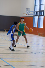 Naklejka premium Two male basketball players dribbling orange basketball and defending on gym court with hoop
