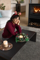 Naklejka premium Woman sitting on floor leaning on coffee table with candle wreath in living room near fireplace