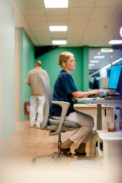 Full length of senior female hospital receptionist working on computer at desk