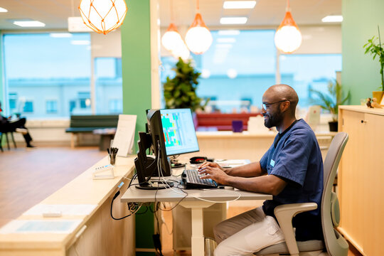 Smiling male receptionist using computer while sitting at reception desk in hospital