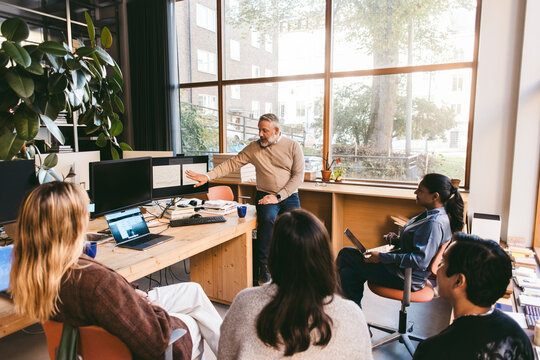 Male business expert explaining ideas on computers to colleagues in architect office